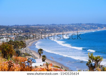 Malibu Beach coastline in California with the blue Pacific Ocean with waves coming in and beach with houses and palm tree's  in background Royalty-Free Stock Photo #1143135614