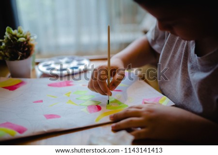 Concept of art, creativity and people. Hand of artist boy with brush painting picture. Child Painting With Watercolor Paints on a White Paper Book.