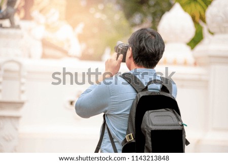 Asian man take a photo at the temple. He carried his bag and held the camera up to take a picture.