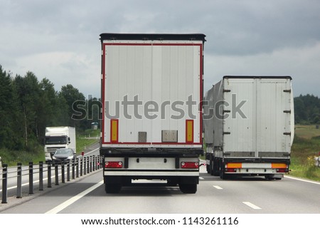 Logistics, international freight by road-two white trucks drive next to the two-lane asphalted country road in the summer day, rear view Royalty-Free Stock Photo #1143261116