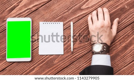 A top view of a hand of a businessman with a tablet PC, pen and notebook on the wooden table. Mock up