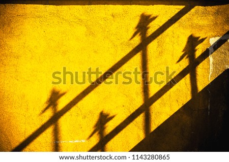 Fence shadow details of four spears on a yellow wall