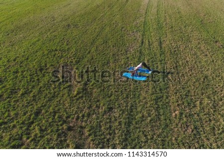 Mom with her little daughter stretching on the mat on the field in warm summer day. Aerial panoramic view.