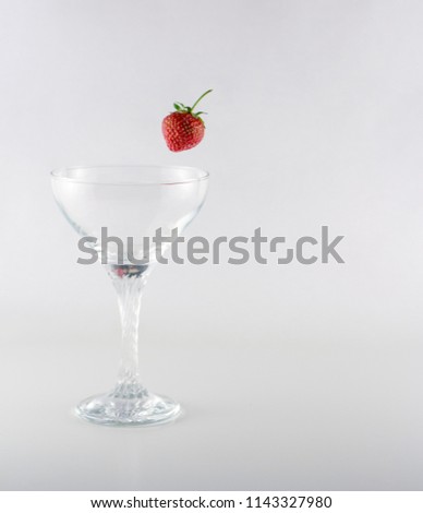 Empty glass with single red strawberry at white background