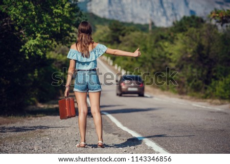 Young beautiful Asian woman in hippy style. travels by hitchhiking. Road in the mountains. The idea and concept of summer holidays and freedom