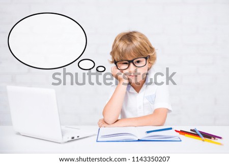 bored little school boy in glasses doing homework at home and thinking about something
