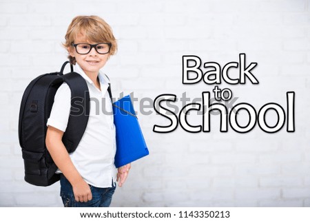 portrait of little school boy in glasses with backpack over white brick wall