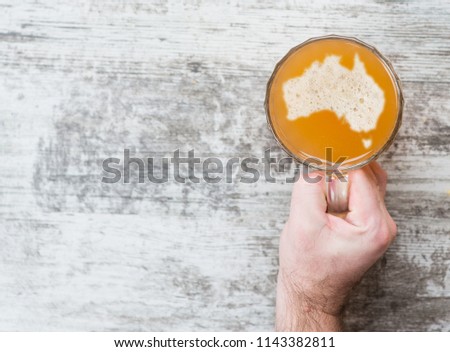 man's hand holds a mug of beer with silhouettes of Australia on foam. Top view. Space for text