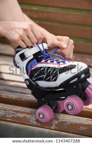 Young stylish woman trying roller skating. Young woman in casual with roller skating on bench in a park. Close up.