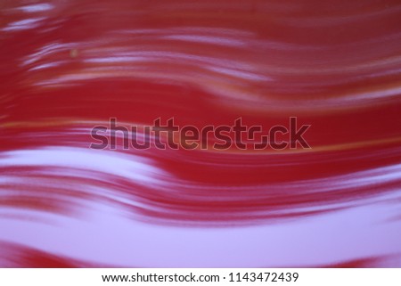 Close up outdoor view of part of the hood of a red car. Bright painted surface with many reflective shapes. Confused drawings in an artistic way. Abstract picture with lines and shadows.