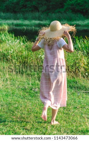 Beautiful, young girl in a pink dress and a straw hat in the field on the grass. Cover, photo for advertising