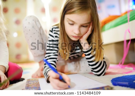 Two cute little sisters writing letters together at home. Older sister helping youngster with her homework. Education for kids.