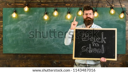 Back to school concept. Teacher in eyeglasses holds blackboard with inscription back to school. Man with beard and mustache on strict face warns students, chalkboard on background.