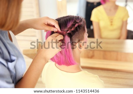 Professional stylist braiding woman's color hair in beauty salon. Modern trend
