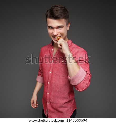 a young guy bites a coin bitcoin with his teeth, checking for authenticity, isolated on a gray background. Royalty-Free Stock Photo #1143533594