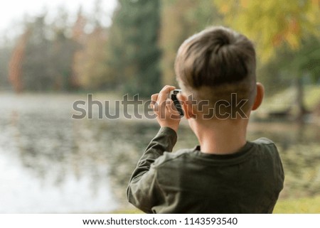 Young boy photographing a lake outdoors in a rear view.
