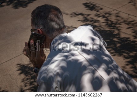 Crescent-shaped shadows fall on a man's back during the 2017 solar eclipse in Dallas, Texas. He's conducting business on a phone during the event.