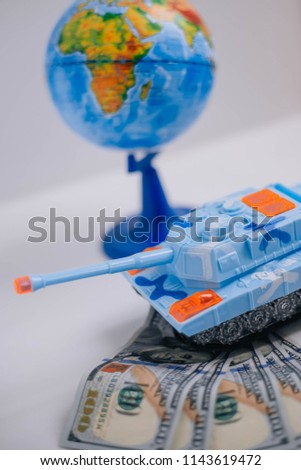 Toy tank, globe in the background, cash. The concept of payment to the military around the world.