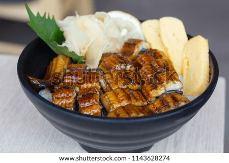 Unagi Don with Sweet Egg on black bowl and wooden table background with copy space.
