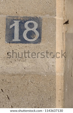 Number eighteen written in white on a blue metallic rectangular plate in a french street. Numerical sign to indicate the address of a house. Isolated element with 18 indicated on a building facade.