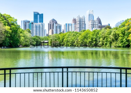Cityscape, skyline view in Piedmont Park in Atlanta, Georgia green foliage, trees, scenic water, urban city skyscrapers downtown at Lake Clara Meer by railing