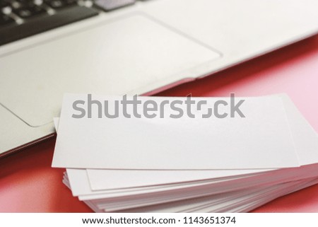 Selective focus of blank business cards and computer laptop on pink color background for workspace concept