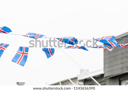 Isolated against cloudy, overcast, white sky many Icelandic national flags on rope in Reykjavik on street with buildings, raining rain water drops