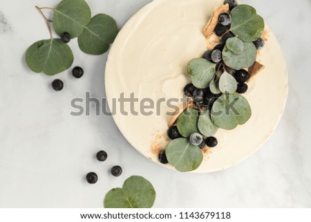 White chocolate cheesecake non baked on a grey plate and marble table. Garnishes with green leaves and black berries for presentation. Neutral flat lay colored.