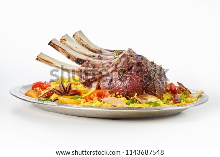 Grilled rack of spicy Oriental lamp chops served on couscous with roasted vegetables seasoned with herbs and spices viewed low angle on an oval plate on white Royalty-Free Stock Photo #1143687548
