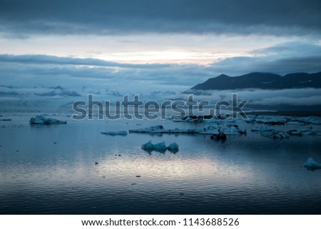 Bluish picture of Glacier Lagoon in Iceland with low altitude clouds and glacier moraine in the background.