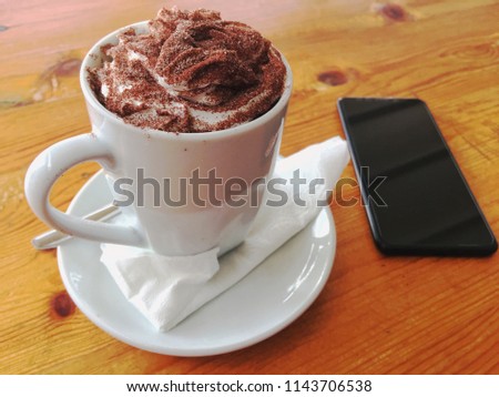 above view of Smart phone and cup of latte art coffee cappuccino with chocolate cream on wooden background