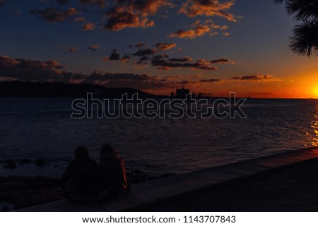 two people sitting on the riverbank admiring the beautiful sunset. blue and orange shades of the sky and silhouettes of the opposite shore