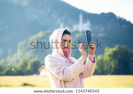 Girl doing selfie on her smartfone, traveler woman making pictures with castle view
