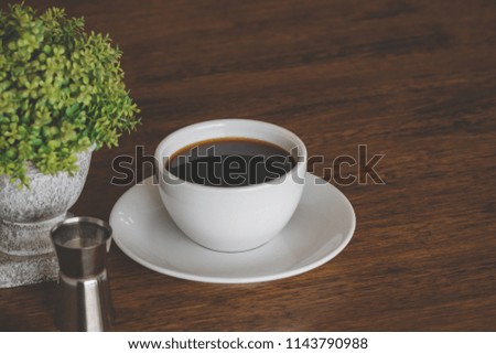 White coffee cup on wood table. with syrup shot. near a potted plant