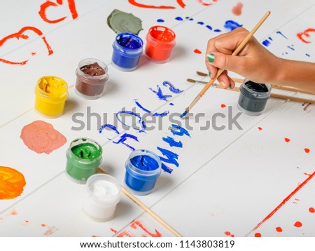 The girl draws messy signs on a wooden table.