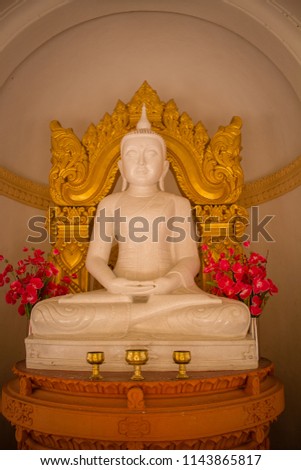 White buddha statue with gold decoration at the back with pink flowers decorate and worship