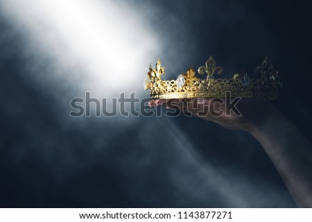 mysteriousand magical image of woman's hand holding a gold crown over gothic black background. Medieval period concept Royalty-Free Stock Photo #1143877271