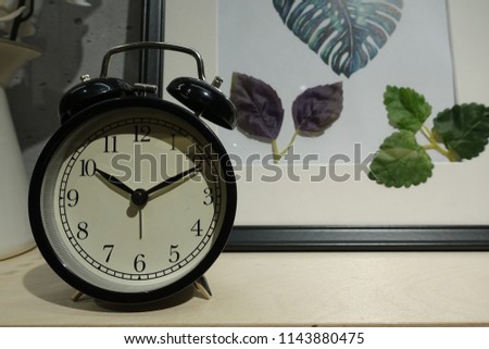 Closeup alarm clock for decorate around things for interior decoration design on wood desk and wall textured with photo frames decoration background