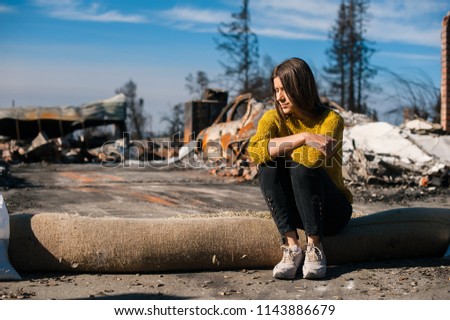 Young owner woman checking burned ruined house and yard after fire, consequences of fire disaster accident. Ruins after fire disaster, loss and despair concept.