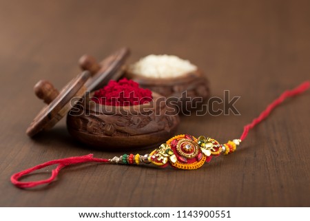 Indian festival: Raksha Bandhan background with an elegant Rakhi, Rice Grains and Kumkum. A traditional Indian wrist band which is a symbol of love between Brothers and Sisters. Royalty-Free Stock Photo #1143900551