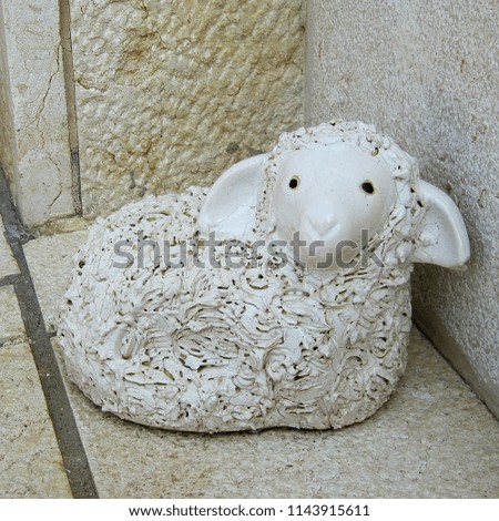 Statuette of white stone in the shape of a small lamb on the wall background
