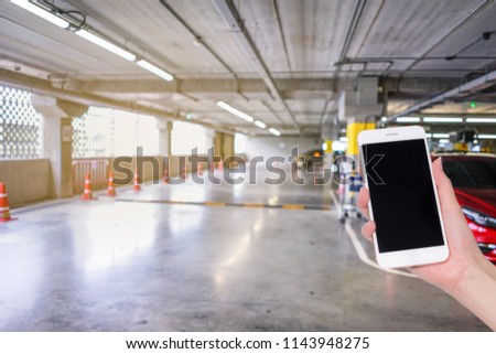 Hand holding mobile phone with indoor parking lot building blurred background and bokeh light