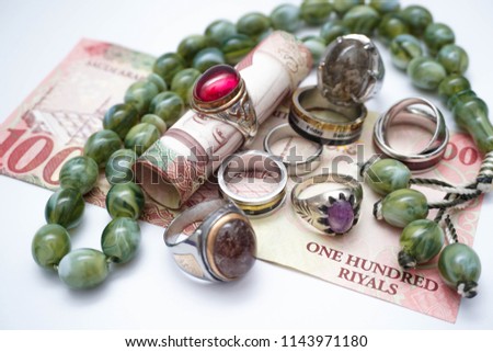 rosary, rings and Saudi Riyals bank notes with makkah , medina , riyadh landmarks. Coins designed to show religious tourism supporting financial investment opportunities
