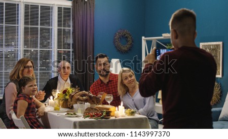 Teen boy with parents and grandparents and sister at table on Thanksgiving day and taking photo together using smartphone