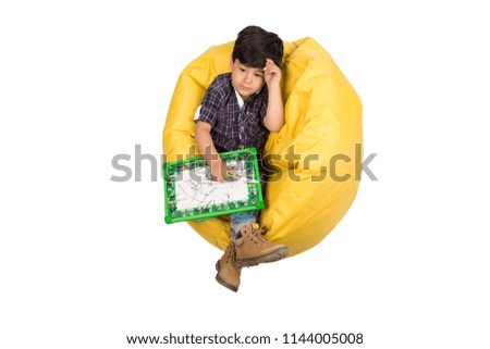 cute child thinking and holding writing board , sitting on beanbag , isolated on white background