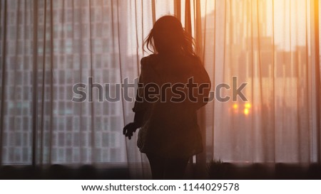 Silhouette of young woman goingto open curtains on building on the background in the window