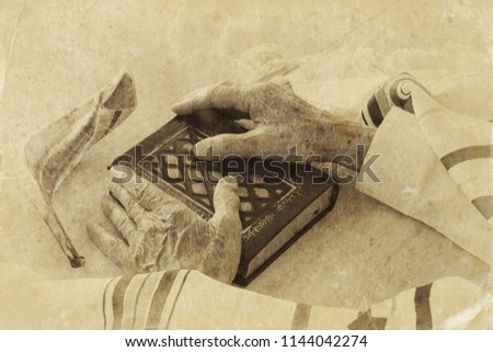 Old Jewish man hands holding a Prayer book, praying, next to tallit and shofar (horn). Jewish traditional symbols. Rosh hashanah (jewish New Year holiday) and Yom kippur concept Royalty-Free Stock Photo #1144042274