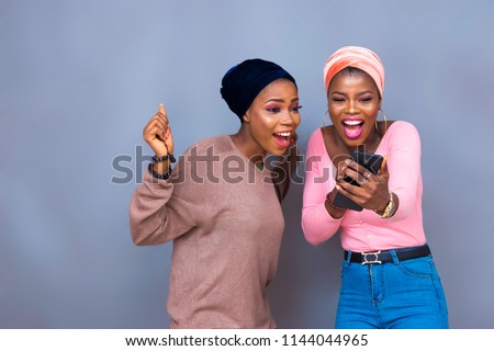 excited girls looking at a phone. young black girls very excited while holding and looking at a phone. Royalty-Free Stock Photo #1144044965