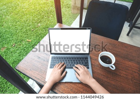 Top view mockup image of a woman using and typing on laptop with blank white desktop screen and coffee cup on wooden table and green nature background 