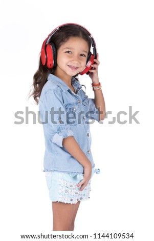 Side shot of cute small girl listening to music on wireless headphones putting her hand on it and smiling, isolated on white background